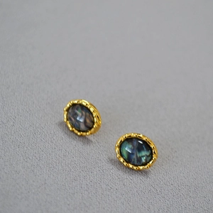 Macro detail of oval brass gold-plated stud earrings featuring iridescent abalone shell