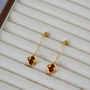 Detail view of golden four-leaf clover earrings with red agate and bamboo texture