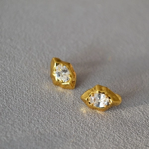 Macro view of gold irregular lava texture earrings with oval-cut zircon in 4-prong setting