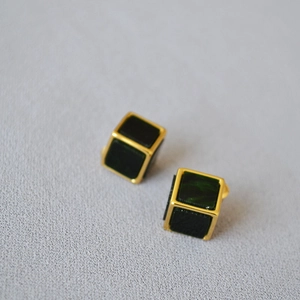 Dettaglio di orecchini geometrici a cubo con montatura dorata e intarsio verde scuro