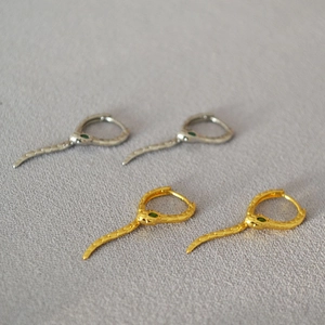 Détail macro de boucles d'oreilles serpent montrant la texture des écailles et yeux verts