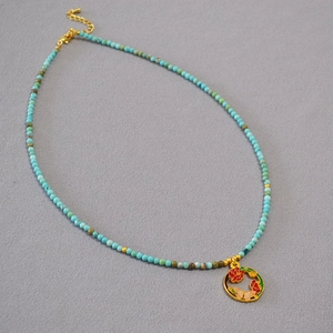 Détail d'un collier en perles turquoise avec pendentif fleur émaillé doré sur tissu gris