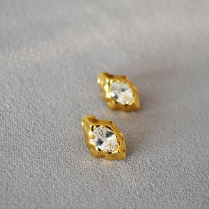 Irregular gold lava stud earrings with oval zircon inlay on grey textured background
