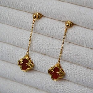 Detail of long gold drop earrings with red clover pendants and bamboo patterns