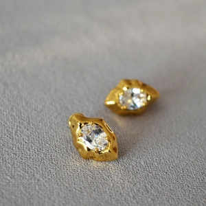 Golden irregular lava style earrings with oval zircon stones on grey textured fabric