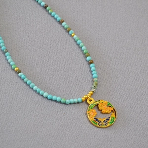 Détail du collier de perles turquoise avec pendentif floral et papillon en émail coloré