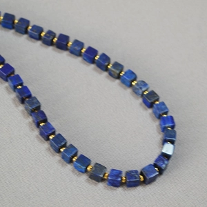 Close-up of lapis lazuli square beads necklace with gold spacers on grey fabric