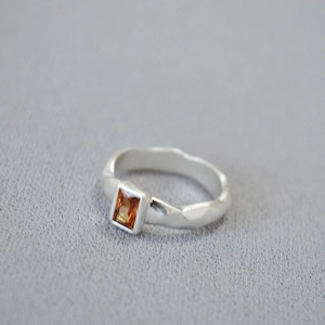 Detail of silver textured ring featuring a rectangle amber-colored zircon gemstone