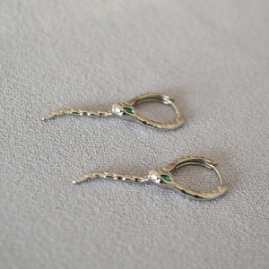 Vue détaillée des boucles d'oreilles serpent argentées avec yeux en pierres vertes