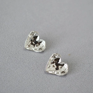 Detail of silver heart-shaped stud earrings with unique irregular hammered metal texture