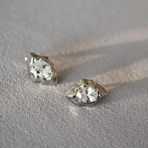 Detail of silver lava-style stud earrings with oval zircon stone on a textured surface