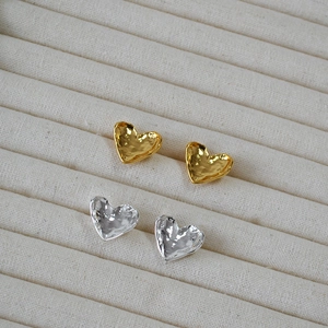 Detail of gold and silver heart-shaped earrings with unique hammered metal texture