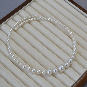 Elegant white faux pearl choker necklace with gradient bead design on beige velvet display