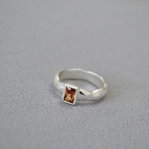 Detail of hammered silver metal ring with a rectangular orange-yellow zircon stone
