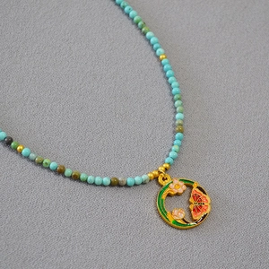 Détail macro du collier en perles turquoise avec pendentif en émail floral fait main