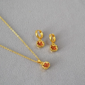 Detail of gold-plated jewelry set with pomegranate-shaped red gemstones and cross chain