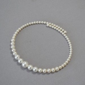 Detail view of graduated imitation pearl choker with creamy white luster on grey fabric