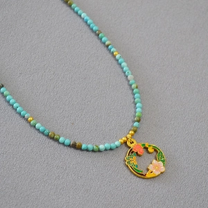 Détail du collier de perles turquoise avec un pendentif floral en émail artisanal
