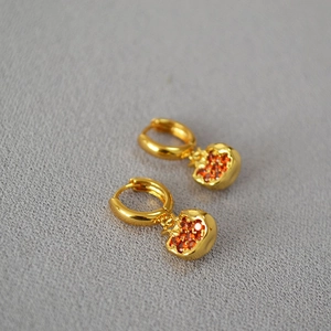 Detailed view of gold pomegranate earrings with pave-set red stones on grey fabric