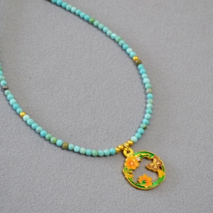 Détail du collier de perles turquoise avec pendentif en émail doré fleur et papillon