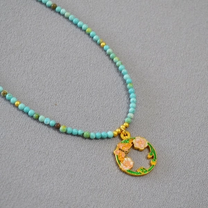 Détail du pendentif fleur papillon en émail et du collier de perles turquoise