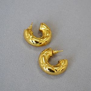 Detailed view of gold-plated quilted C-shaped hoop earrings on grey textured background