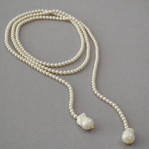 Close-up of long pearl necklace featuring large baroque drops and golden bead accents