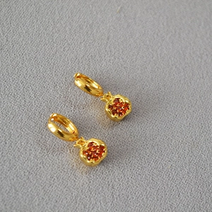Detailed close-up of pomegranate-shaped gold earrings with sparkling red crystals