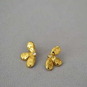 Détail de boucles d'oreilles pétales dorés avec texture martelée et pierre de zircon