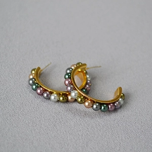 Detail of gold-tone C-shaped hoop earrings featuring two rows of colorful beaded accents