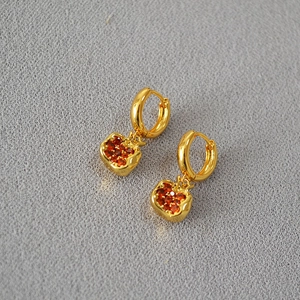 Detail of gold-plated apple earrings with shimmering red gemstones on a grey surface