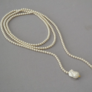 Detail view of long French pearl necklace with baroque pendant on grey fabric