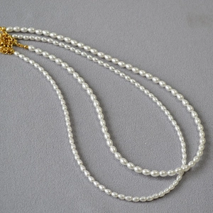 Collier double rang de perles ovales blanches avec fermoir mousqueton doré sur tissu gris
