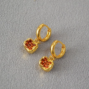 Macro detail of gold-plated apple earrings with pavé-set red cubic zirconia crystals
