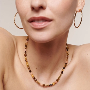 Tiger eye beaded necklace with textured gold hoop earrings on a fashion model