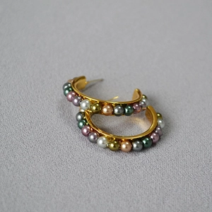Close-up of C-shaped gold earrings with colorful metallic beads on grey fabric