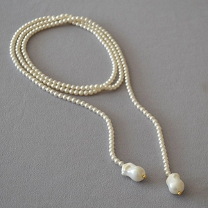 Detail of baroque pearl sweater necklace with irregular pendant on grey linen surface