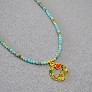Détail du pendentif émaillé papillon fleuri et du collier de perles en turquoise
