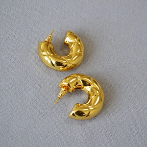 Detail of gold hollow C-shaped earrings featuring a classic quilted rhombic texture