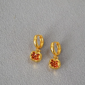 Detail view of gold hoop earrings with red pomegranate charms and red stones