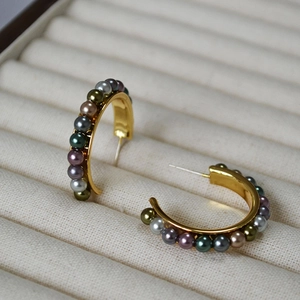 Close-up of C-shaped gold earrings with colorful pearls in a beige jewelry box