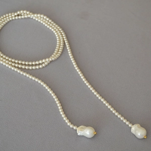 Long white pearl necklace featuring large Baroque teardrop pearls on a textured background