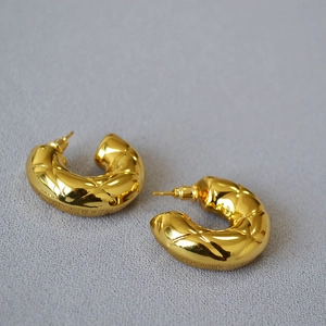 Close-up of gold-plated hollow C-shaped earrings with quilted diamond pattern texture