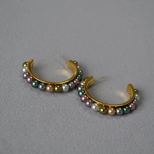 Detail of C-shaped gold earrings with colorful faux pearls on textured grey fabric