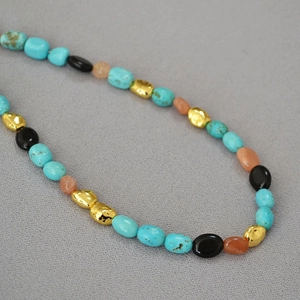 Close-up of vintage turquoise beads and irregular matte golden charms on necklace