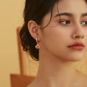 Close-up of elegant gold hoop earrings with a red pomegranate pendant on a model