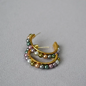 Detail of C-shaped gold earrings with colorful metallic pearls on grey texture