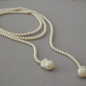 Detailed view of long pearl necklace with large baroque pendants and golden accents
