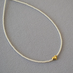 Detail of elegant pearl necklace featuring a polished golden heart pendant on grey background