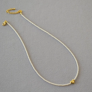 Close-up of minimalist tiny pearl necklace featuring a golden heart pendant and lobster clasp